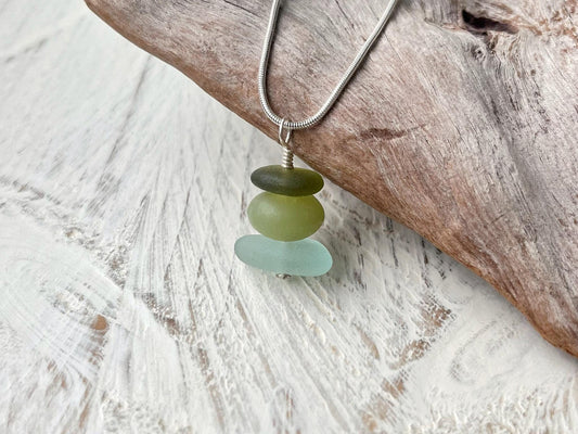 Necklace with green sea glass and a Jade bead sat against driftwood on a textured surface.