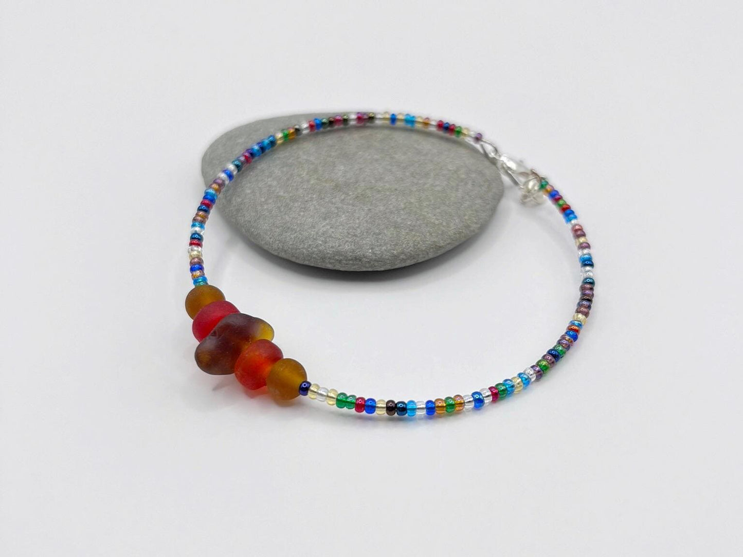Rainbow beaded bracelet with sea glass and frosted glass beads laid on a grey pebble with a white background