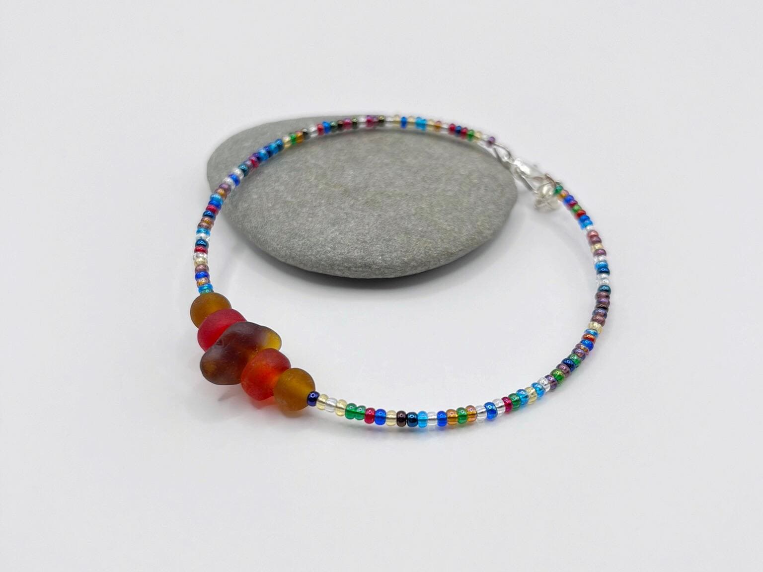 Rainbow beaded bracelet with sea glass and frosted glass beads laid on a grey pebble with a white background
