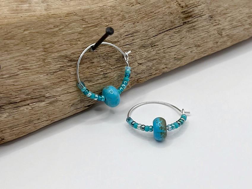 Pair of turquoise beaded hoop earrings hanging on driftwood