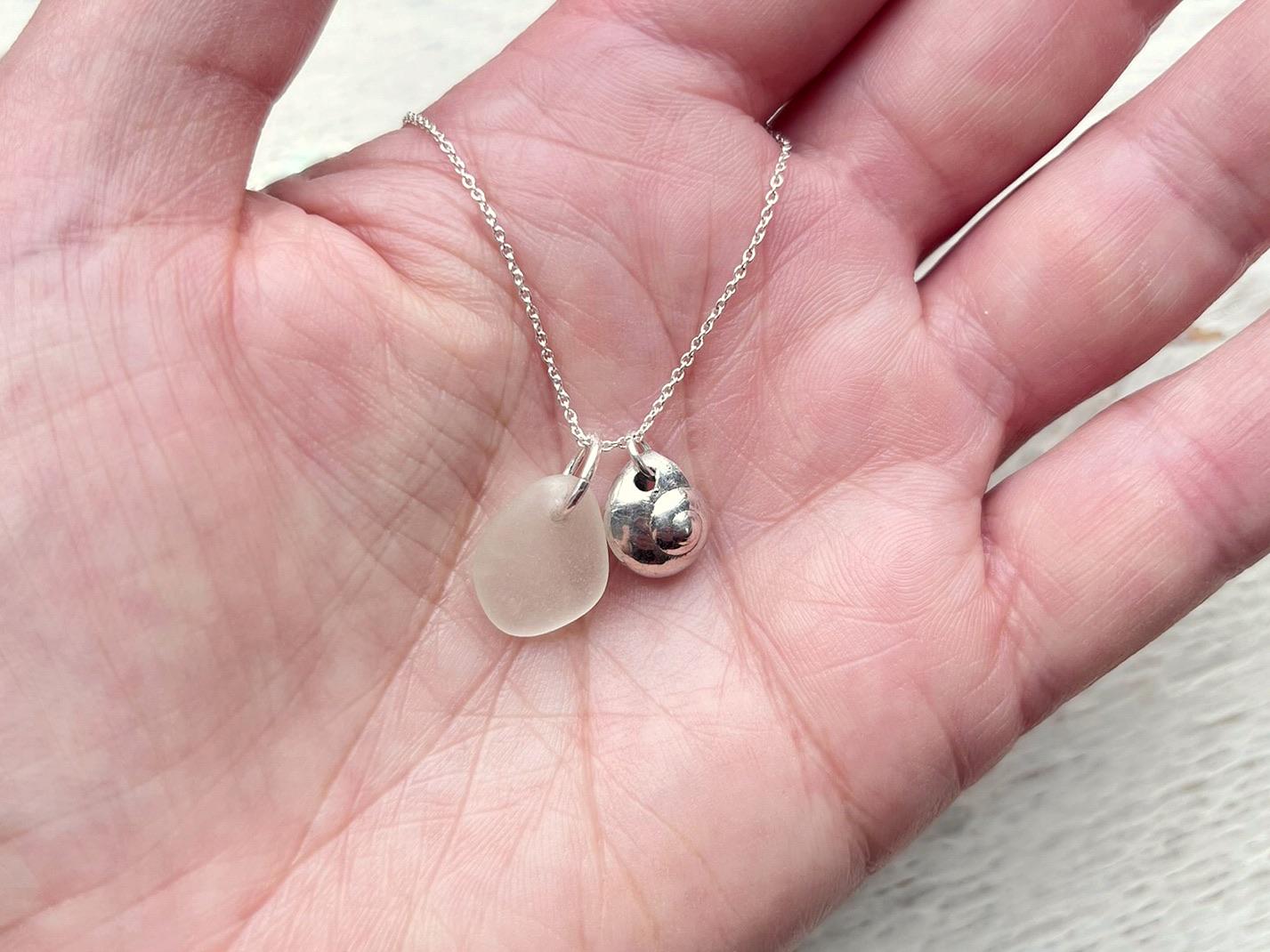 Silver necklace with a silver shell and sea glass pendant held in a hand against a neutral background