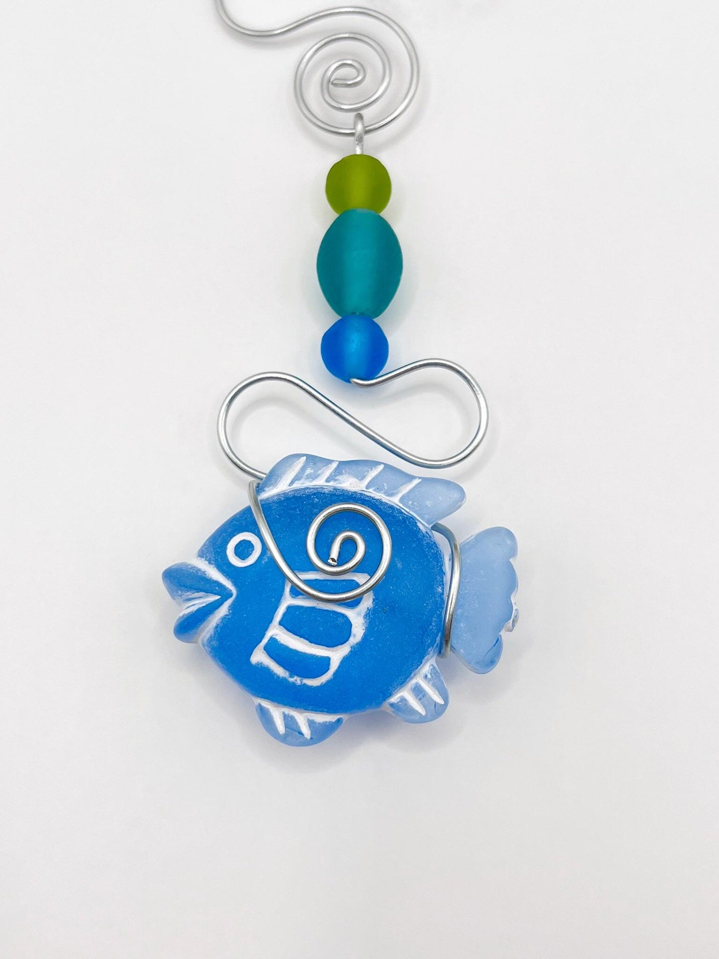 Close up of decorative hanging ornament with blue fish, wire and colourful beads on a white background