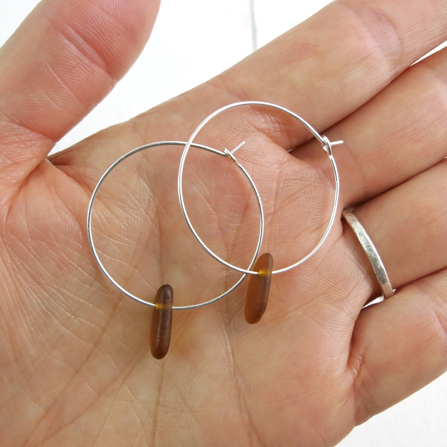 Silver hoop earrings with burnt orange sea glass held in a hand against a white background