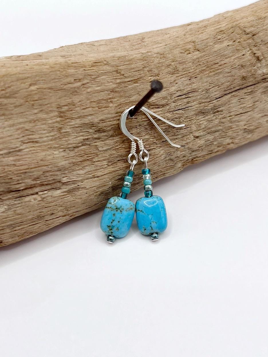 Turquoise earrings on a piece of driftwood with a white background