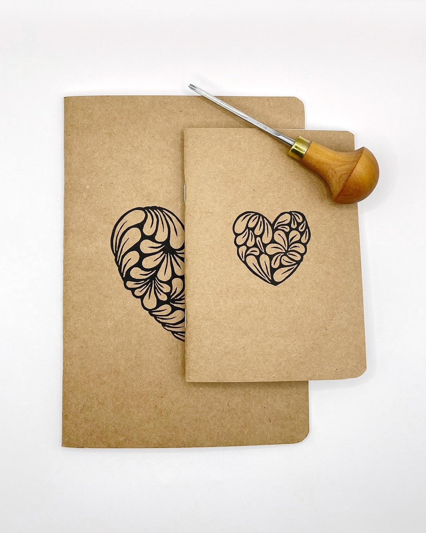 Showing both sizes of the Kraft sketchbooks with lino printed hearts laid on a white background. Photo includes lino cutting oil used 