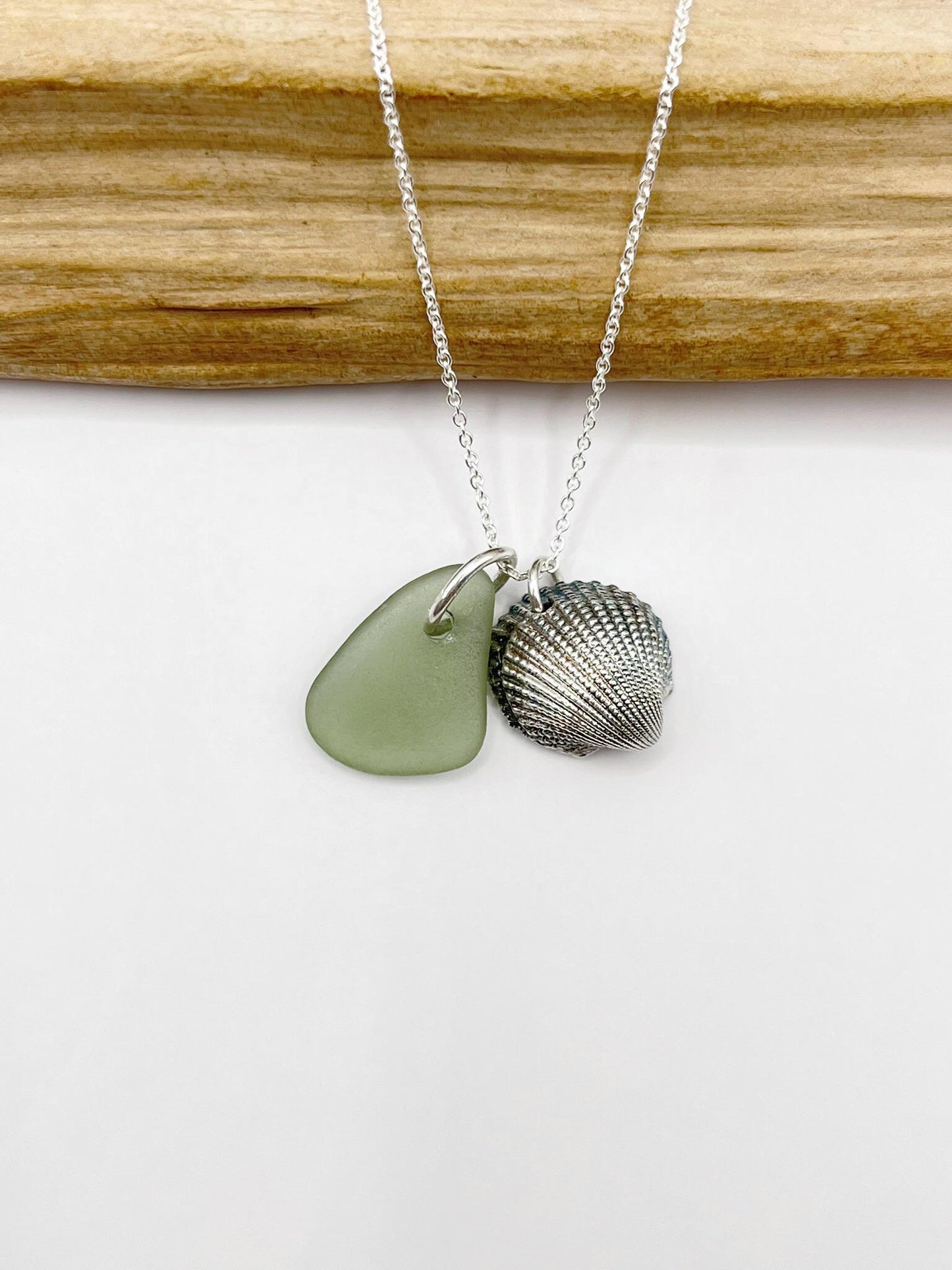 Necklace with green sea glass and a silver shell charm laid on a white background