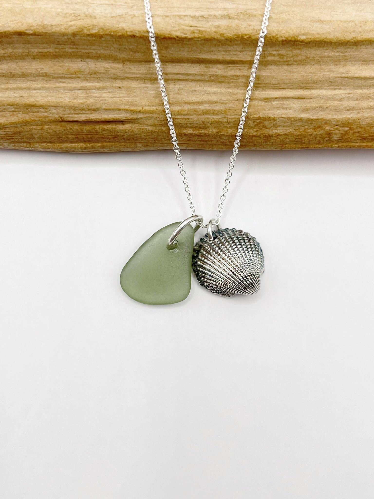 Necklace with green sea glass and a silver shell charm laid on a white background