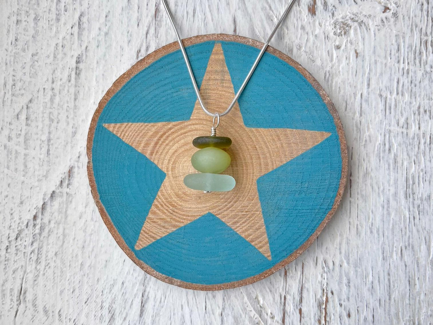 Necklace with green sea glass and a Jade bead laid on a star printed slice of wood against a textured surface.
