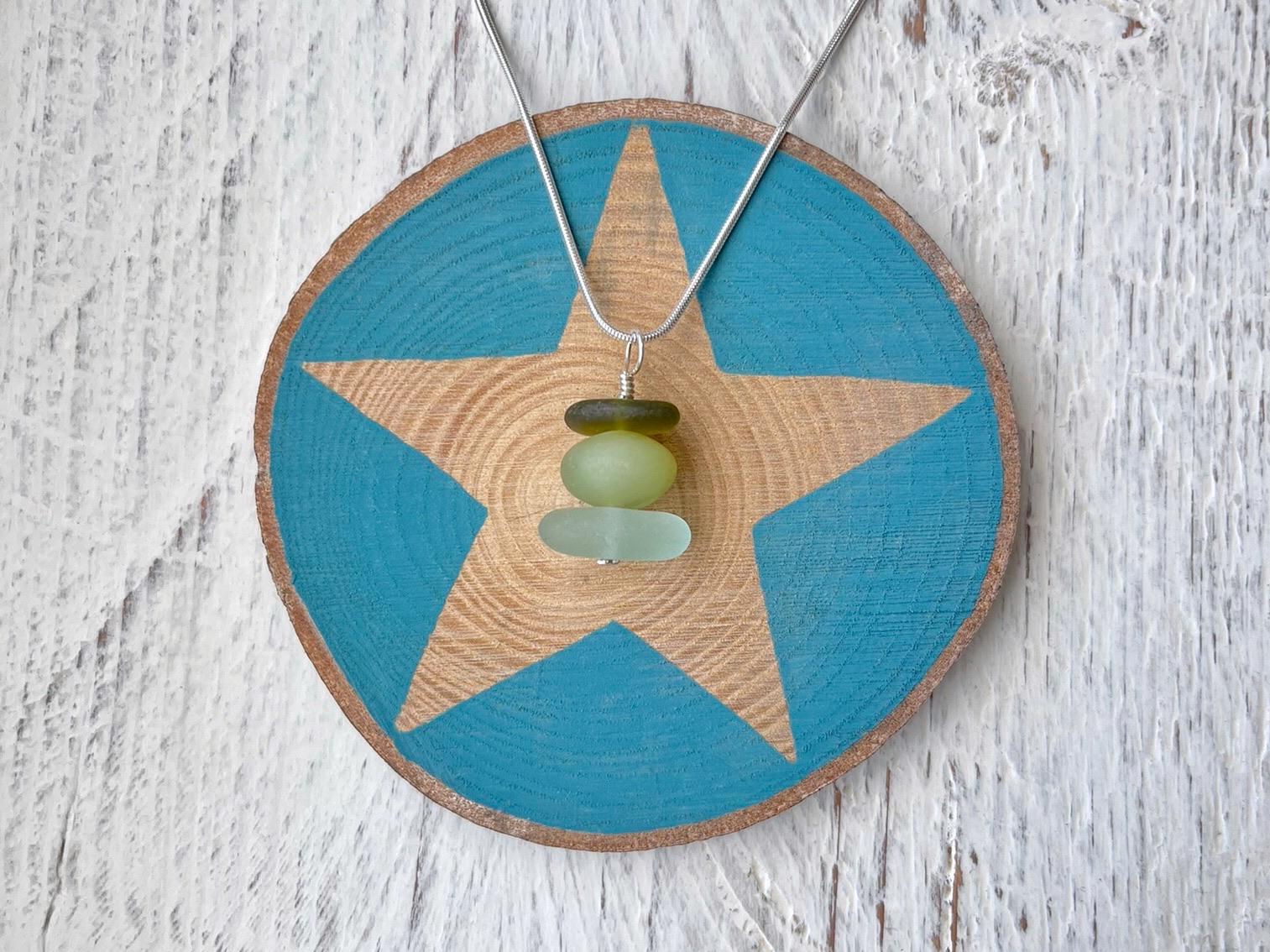 Necklace with green sea glass and a Jade bead laid on a star printed slice of wood against a textured surface.