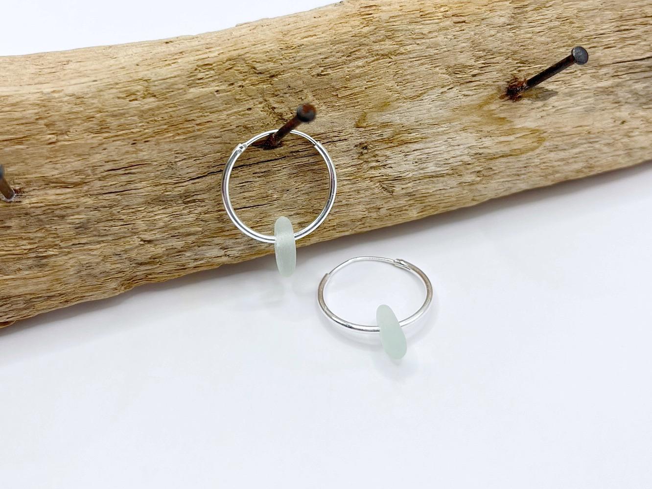 Silver hoop earrings with sea foam coloured sea glass hanging on a piece of driftwood.