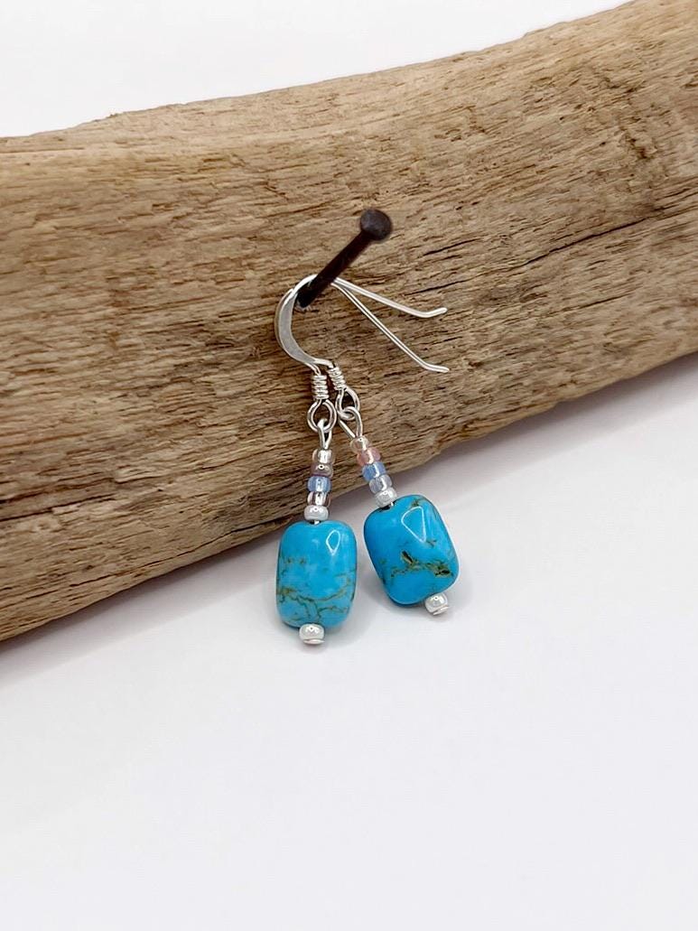 Turquoise earrings with silver hooks on a piece of driftwood.