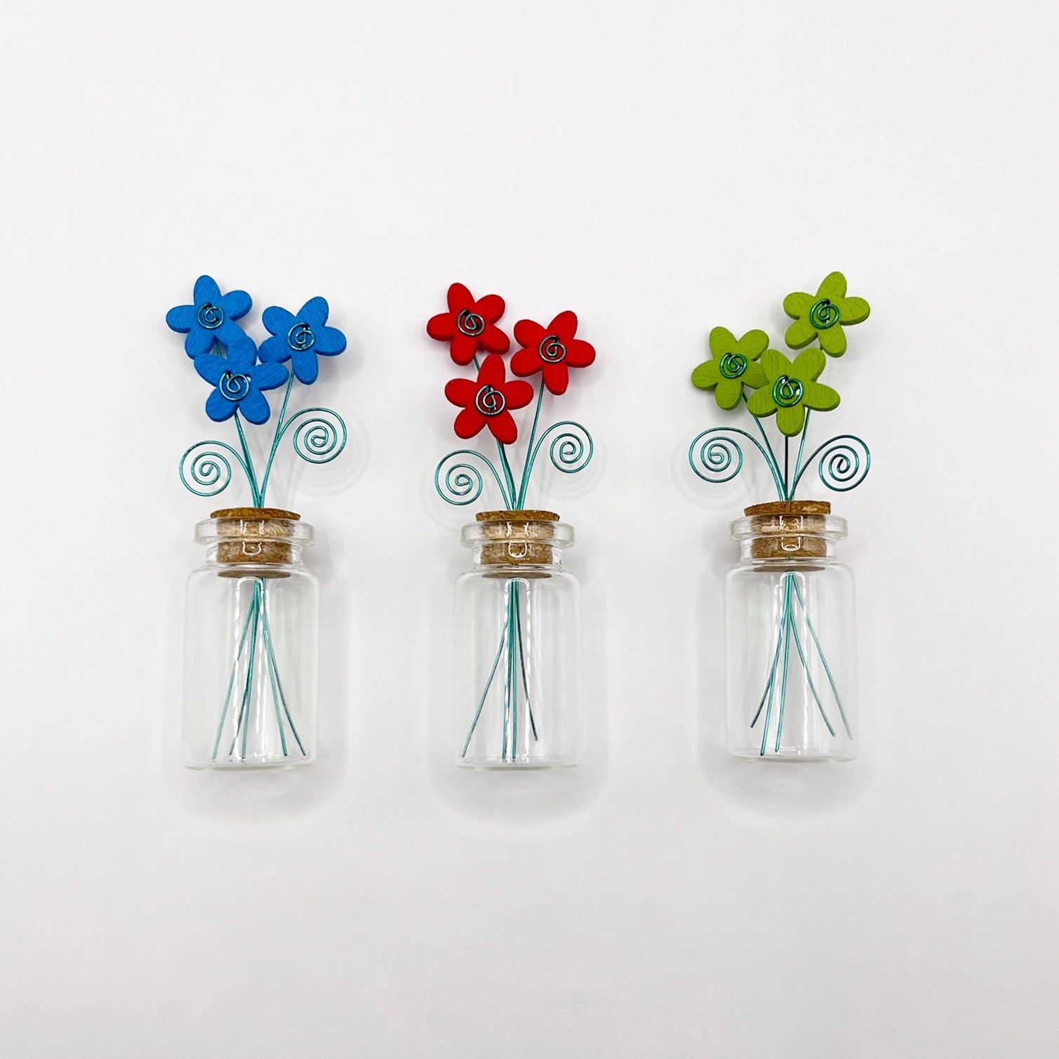 Three little glass bottles with three wooden flowers against a white background