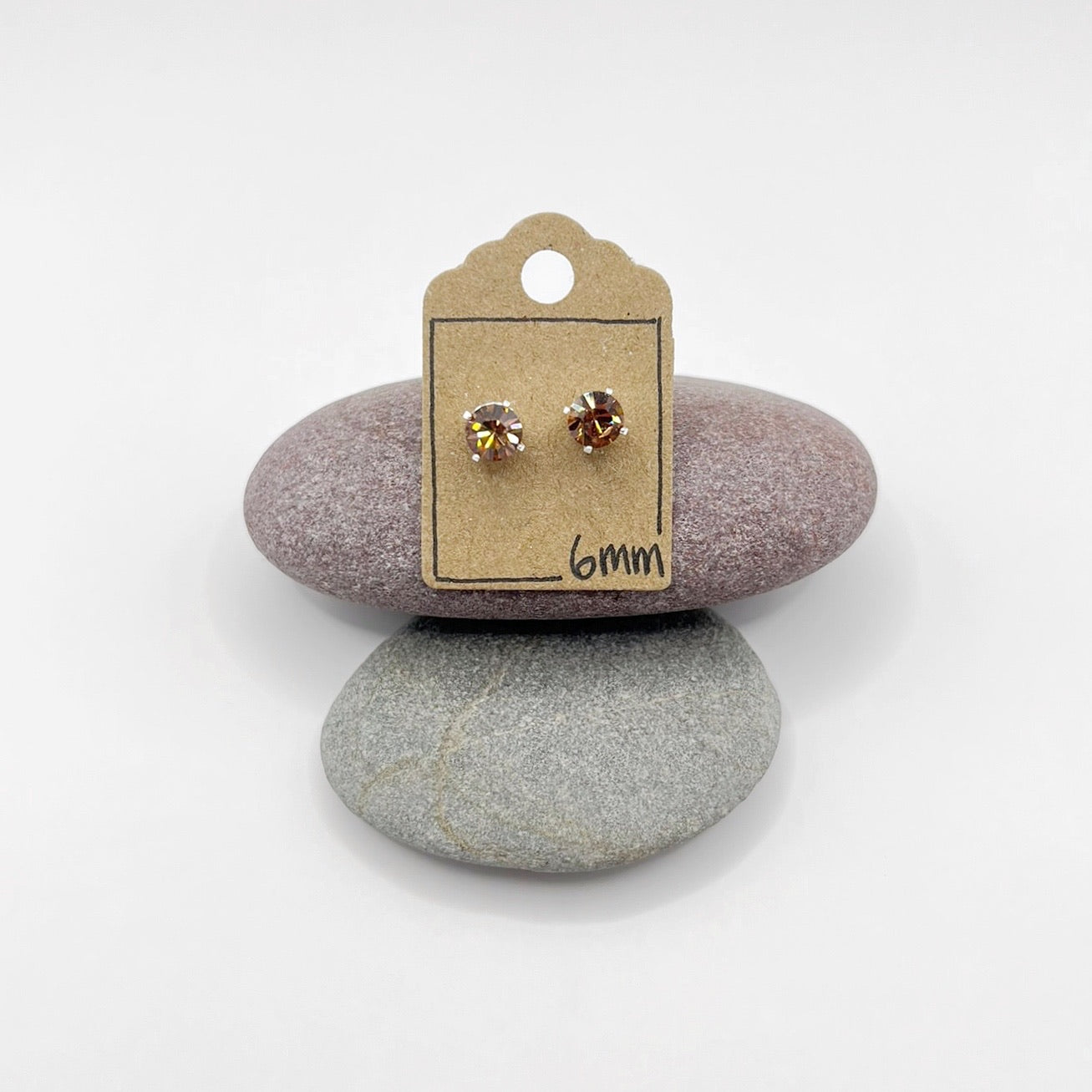 Pair of cut glass stud earrings on a cardboard backing card, placed on two stones with a white background.