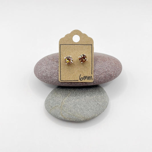Pair of cut glass stud earrings on a cardboard backing card, placed on two stones with a white background.