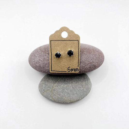 Pair of black stud earrings on a cardboard display card with '5mm' text, placed on two stones.