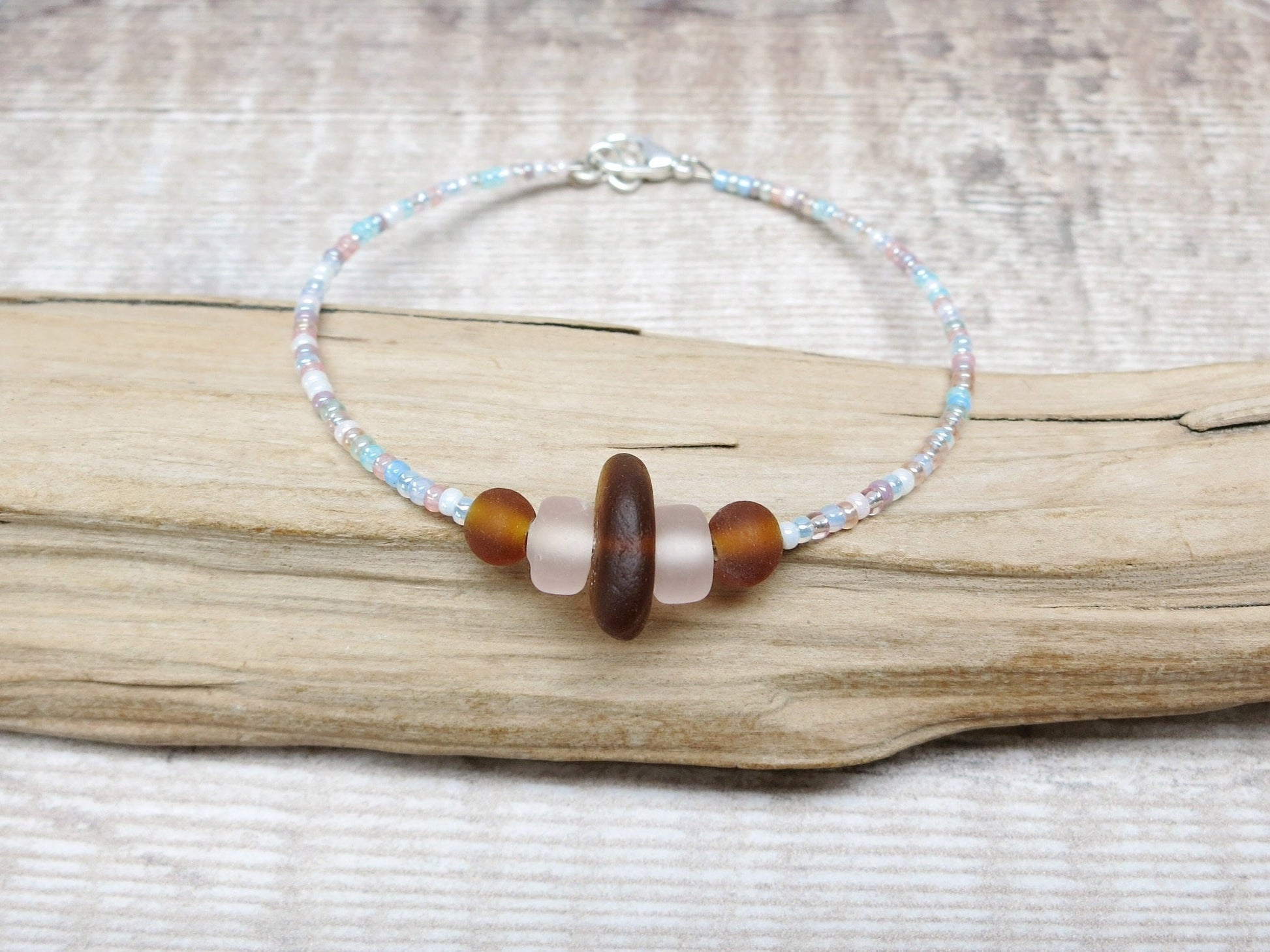Bracelet with pastel seed beads and burnt orange sea glass laid on driftwood.