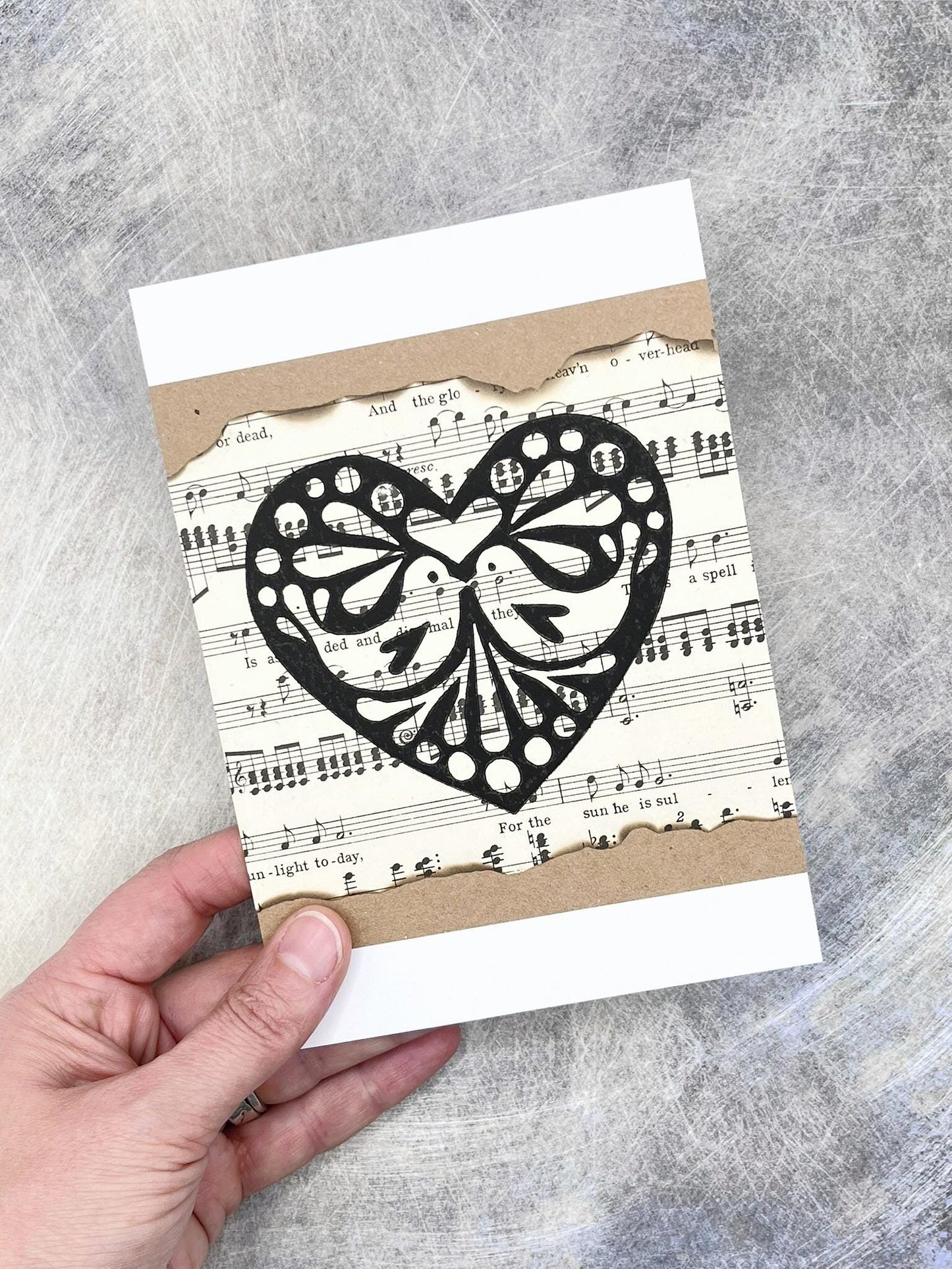 Card with black heart design on sheet music held by a hand against a grey background