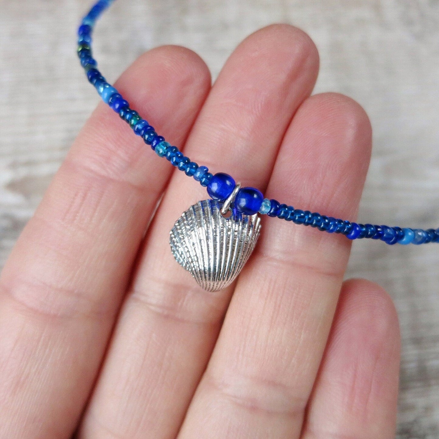 Close up of seed bead necklace with silver coated shell pendants held on fingers against a textured surface
