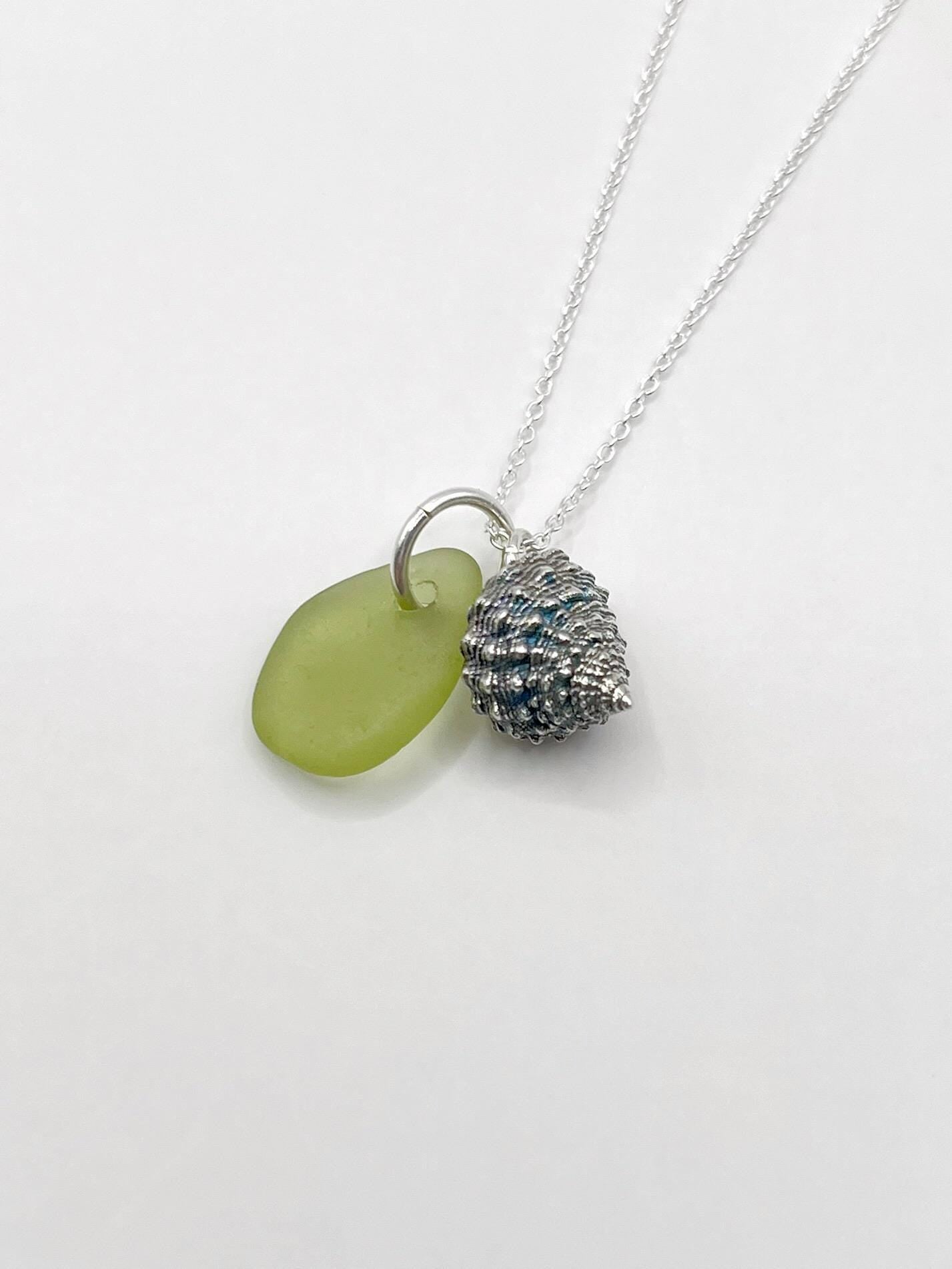 Necklace with lime green sea glass and a a silver shell charm laid on a white background