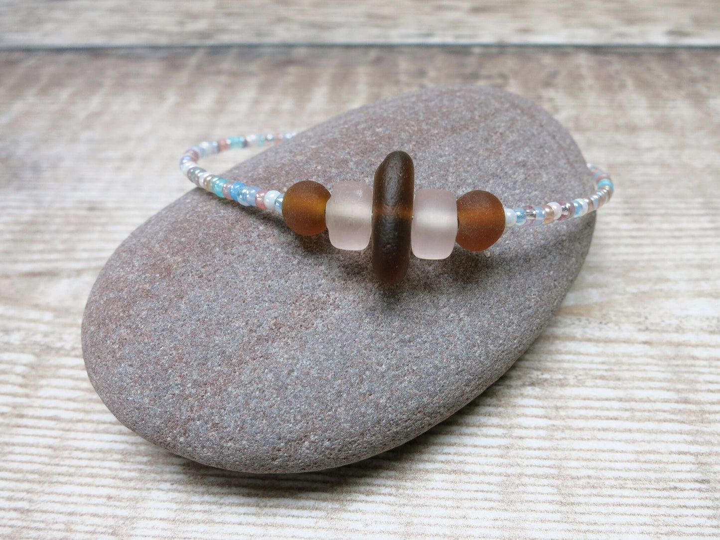 Close up of bracelet with pastel seed beads and burnt orange sea glass laid on a pebble.