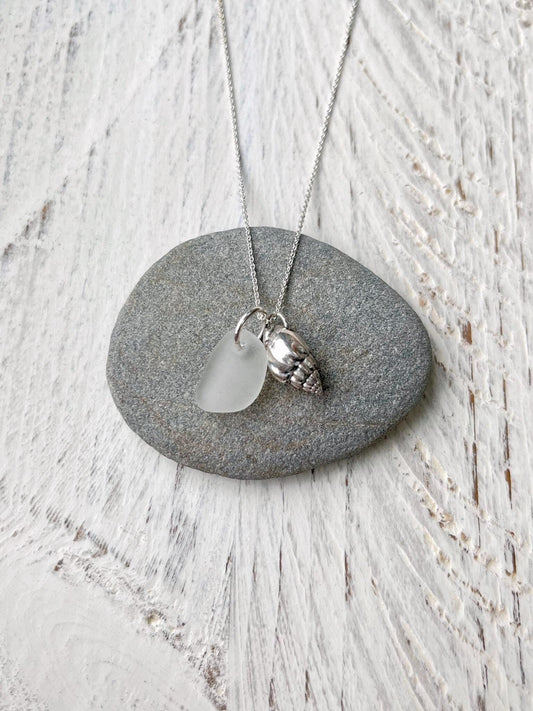 Necklace with white sea glass and silver shell pendant laid on a grey pebble against a textured surface
