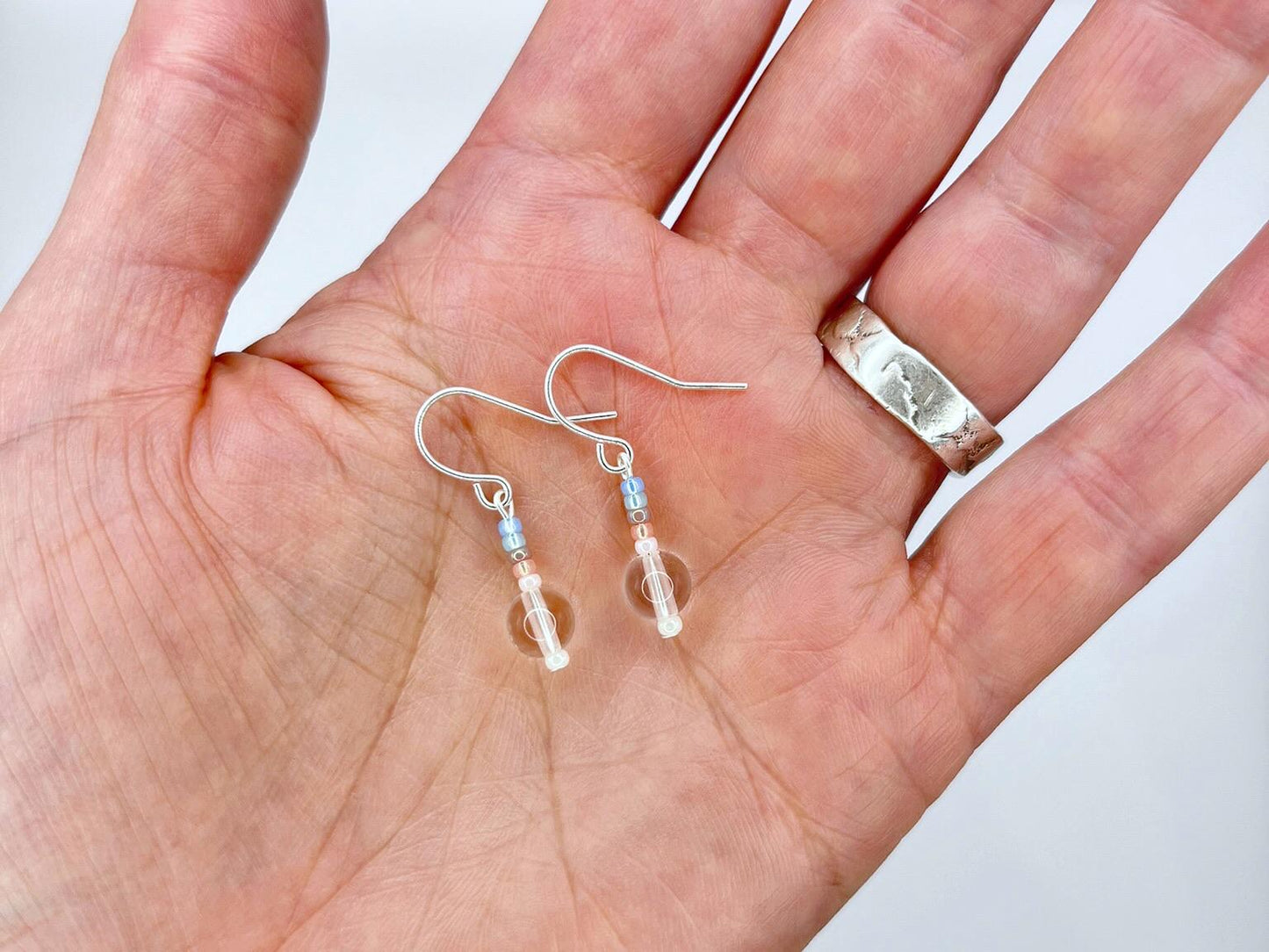 Silver earrings with clear crystal and pastel seed beads held in a hand against a white background