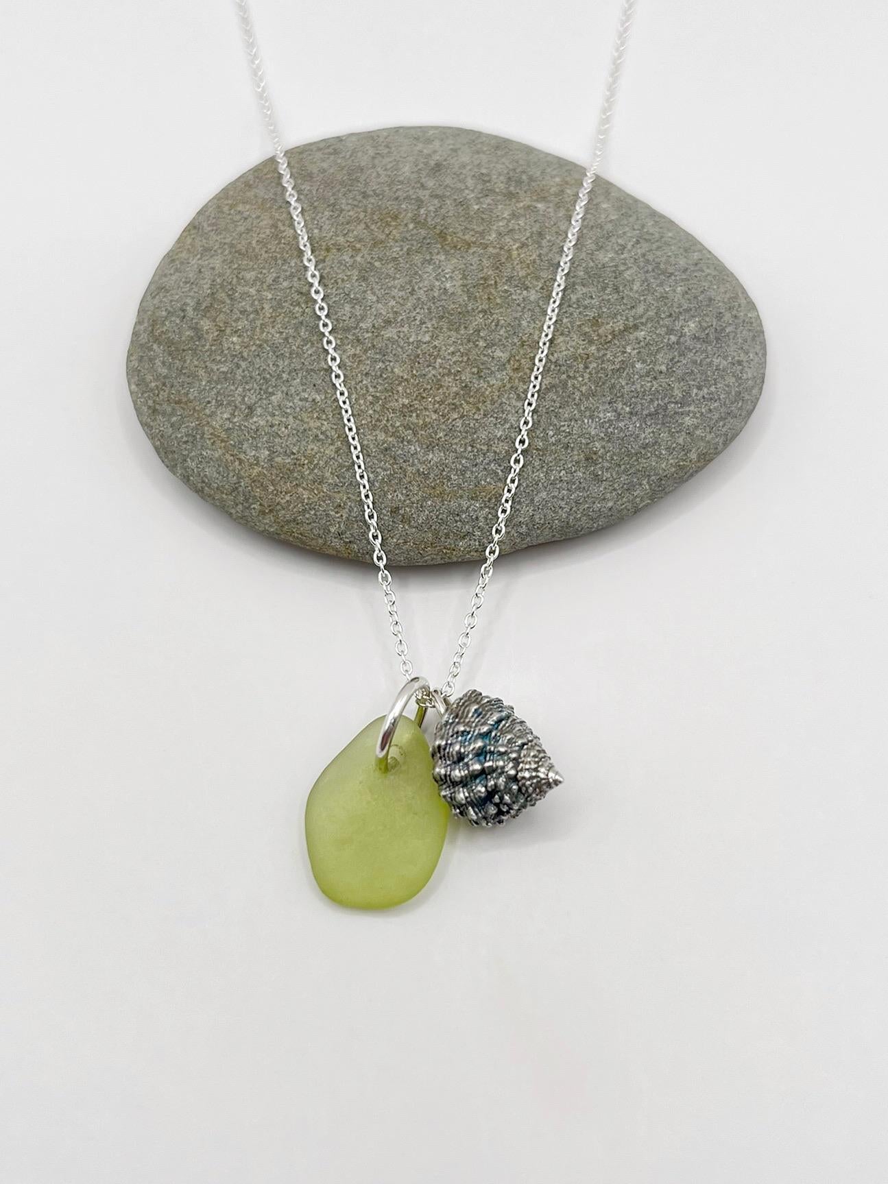 Necklace with lime green sea glass and a silver shell charm laid on a white background