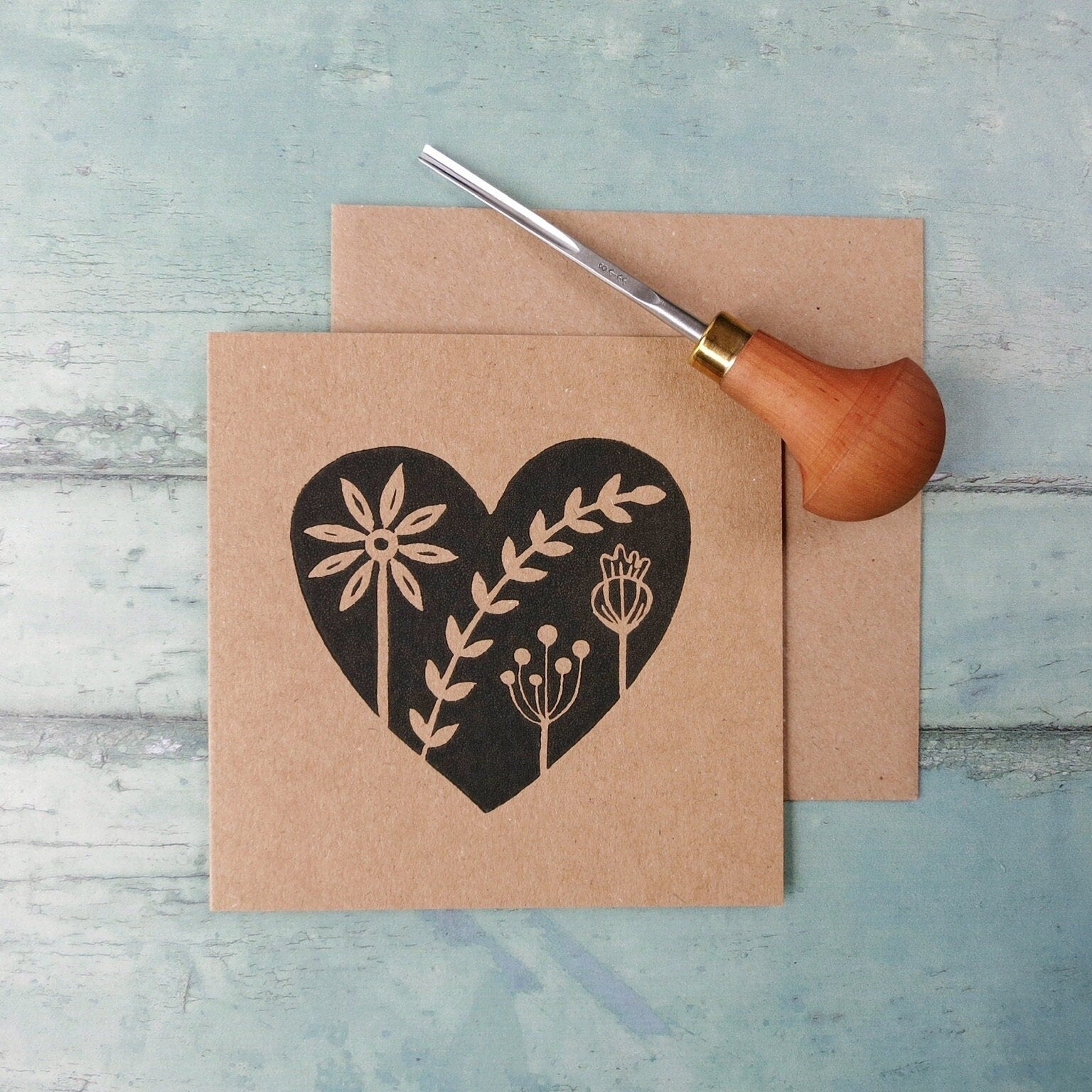 Kraft paper card with an original black lino printed heart design featuring floral elements on a textured surface.