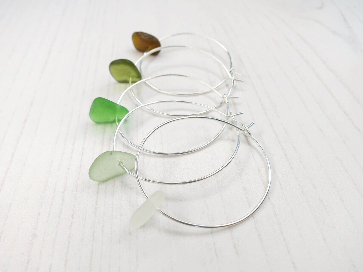 Silver hoop earrings with coloured sea glass laid on a white background