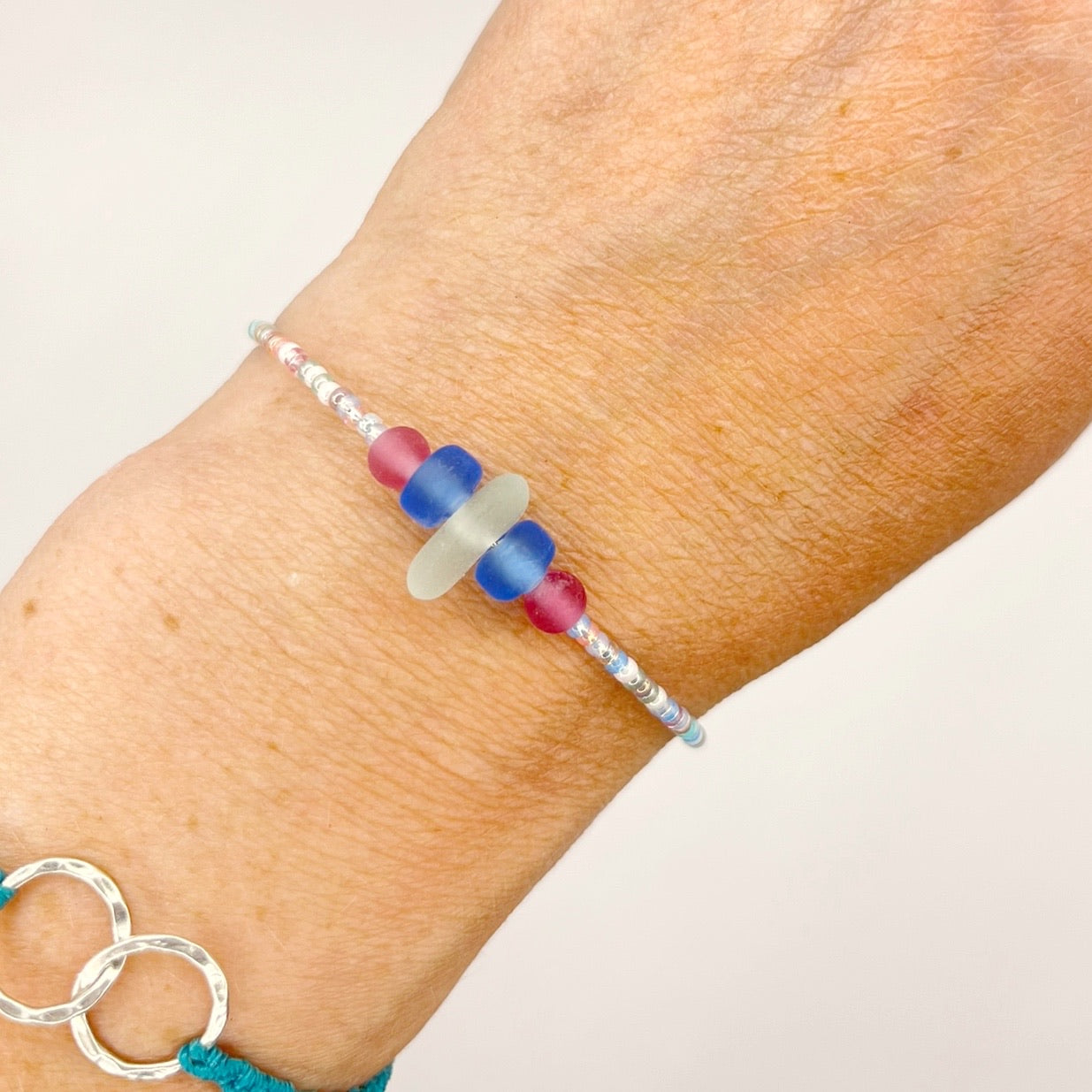 A pastel beaded bracelet with pink and blue frosted glass beads and a piece of sea foam coloured Cornish sea glass, worn on a wrist.