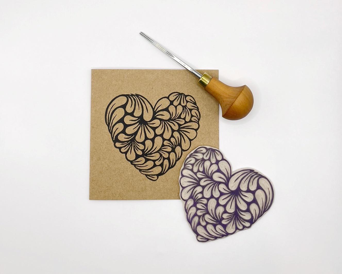 Kraft greetings card with an original lino printed heart laid on a white background. Photo includes lino and cutting tool used.