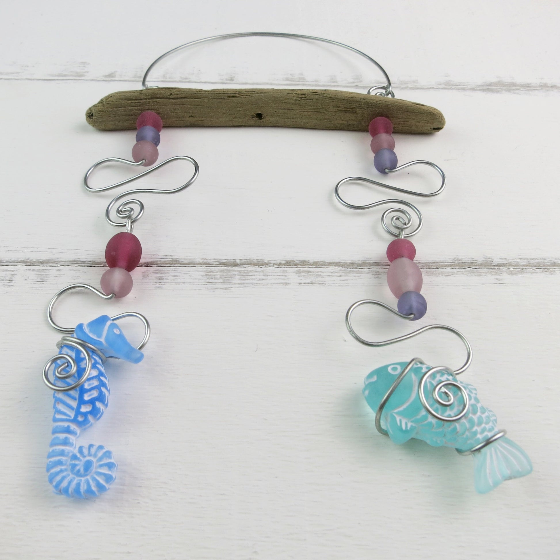 Decorative hanging mobile with a seahorse, fish, glass beads, driftwood and wire on a white wooden background