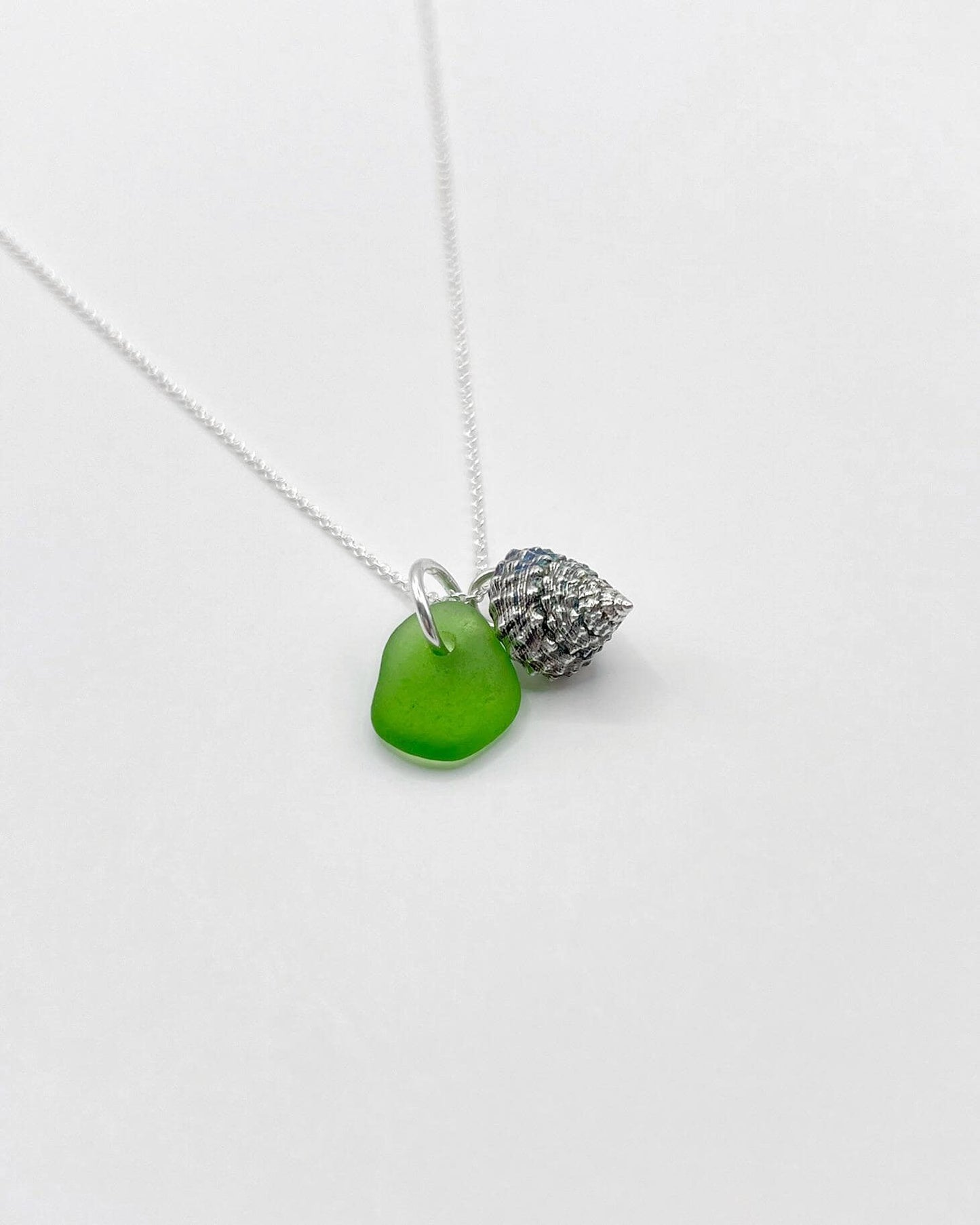 Necklace with green sea glass and silver shell pendant laid on a white background