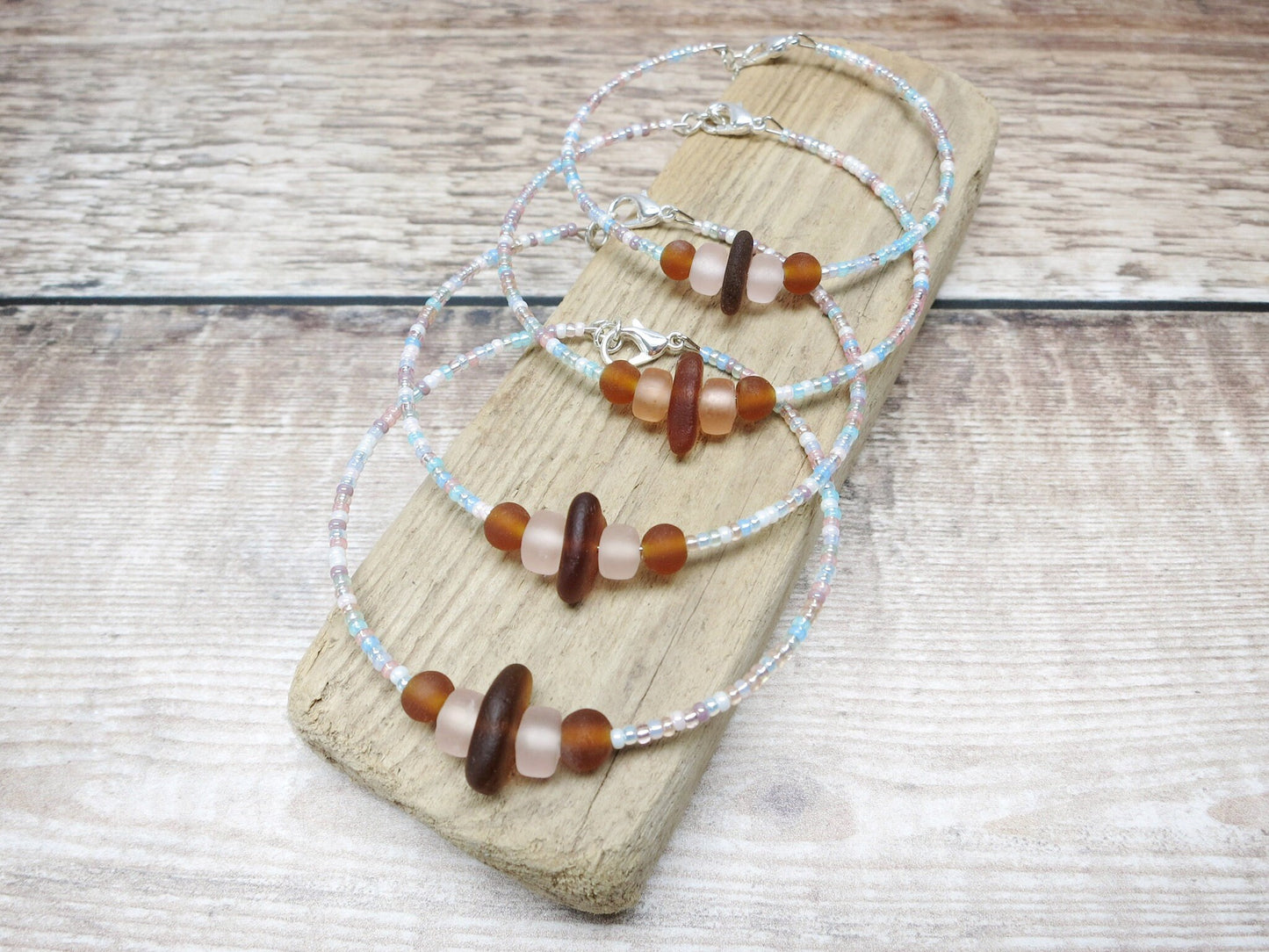 Bracelets with pastel seed beads and burnt orange sea glass laid on driftwood.