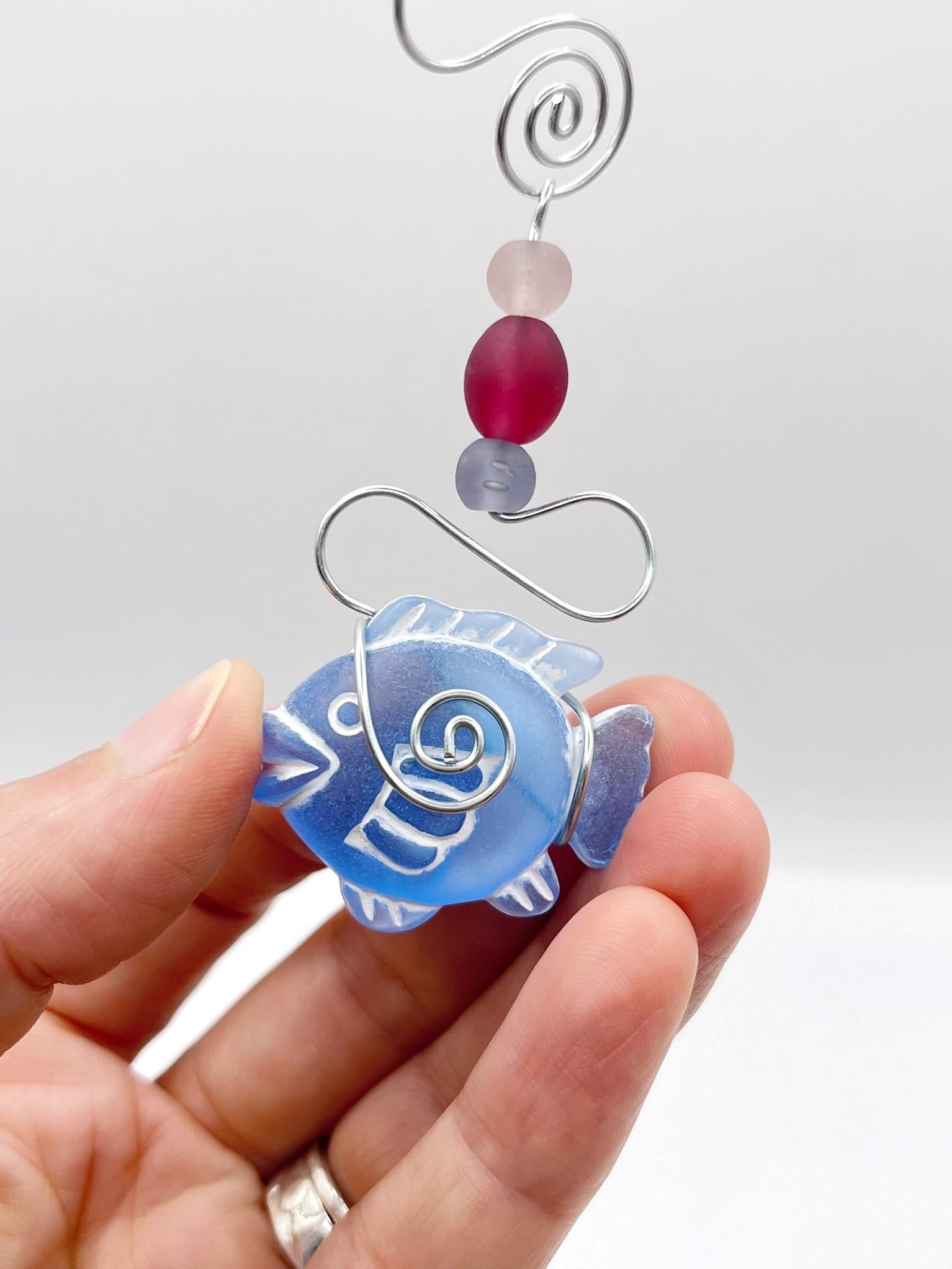 Close up of decorative hanging mobile with blue fish, wire and colourful beads held in a hand against a white background