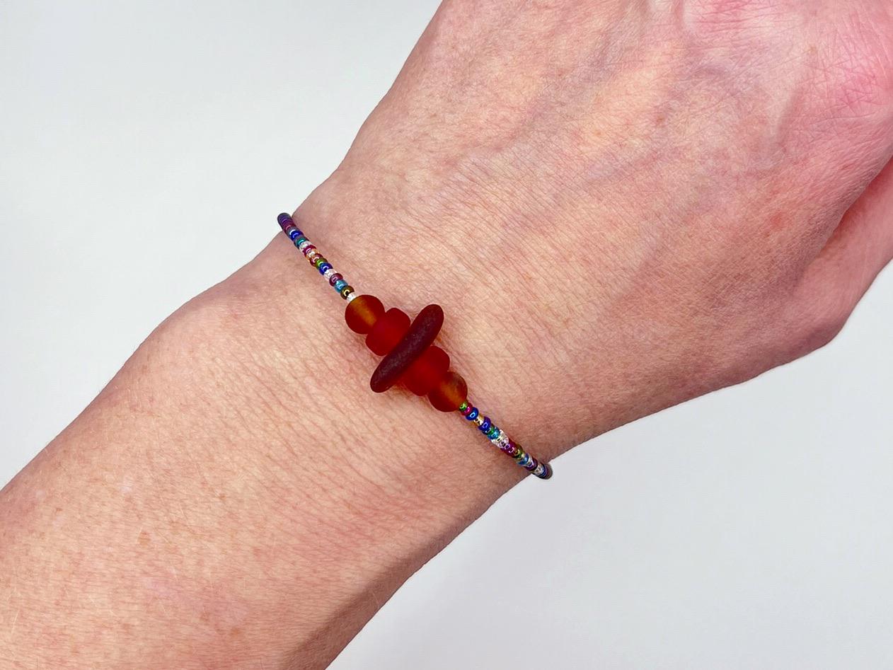 Bracelet with sea glass, rainbow seed beads and frosted glass beads worn on a wrist against a plain background