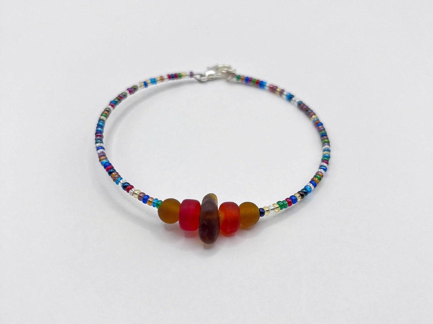 Rainbow beaded bracelet with sea glass and red and brown frosted glass beads laid on a white background