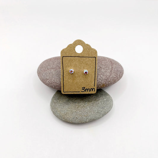 Pair of silver stud earrings on a cardboard backing card with '3mm' marking, placed on two stones.