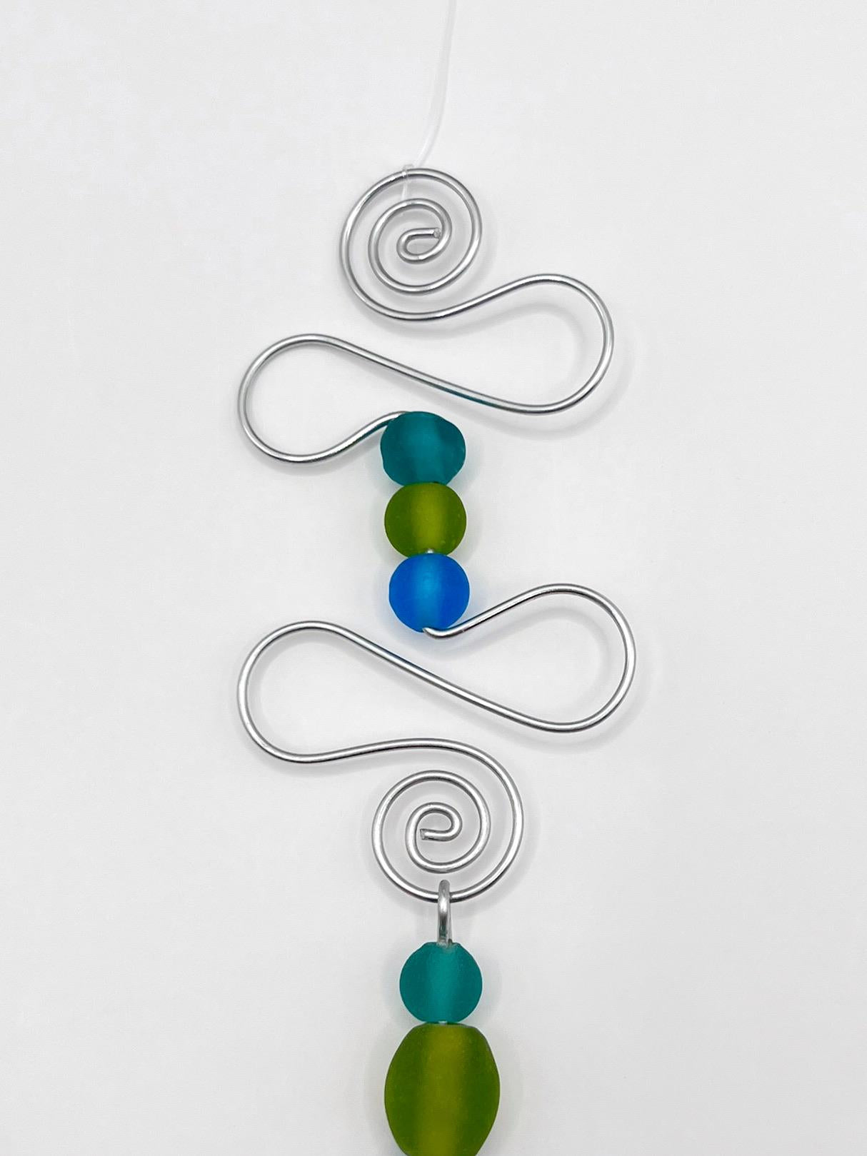 Close up of decorative hanging ornament with blue fish, wire and colourful beads on a white background
