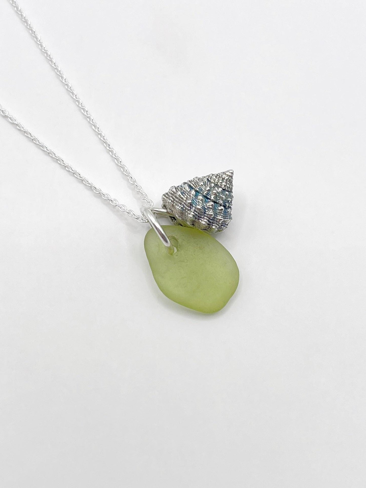 Necklace with lime green sea glass and a silver shell charm laid on a white background