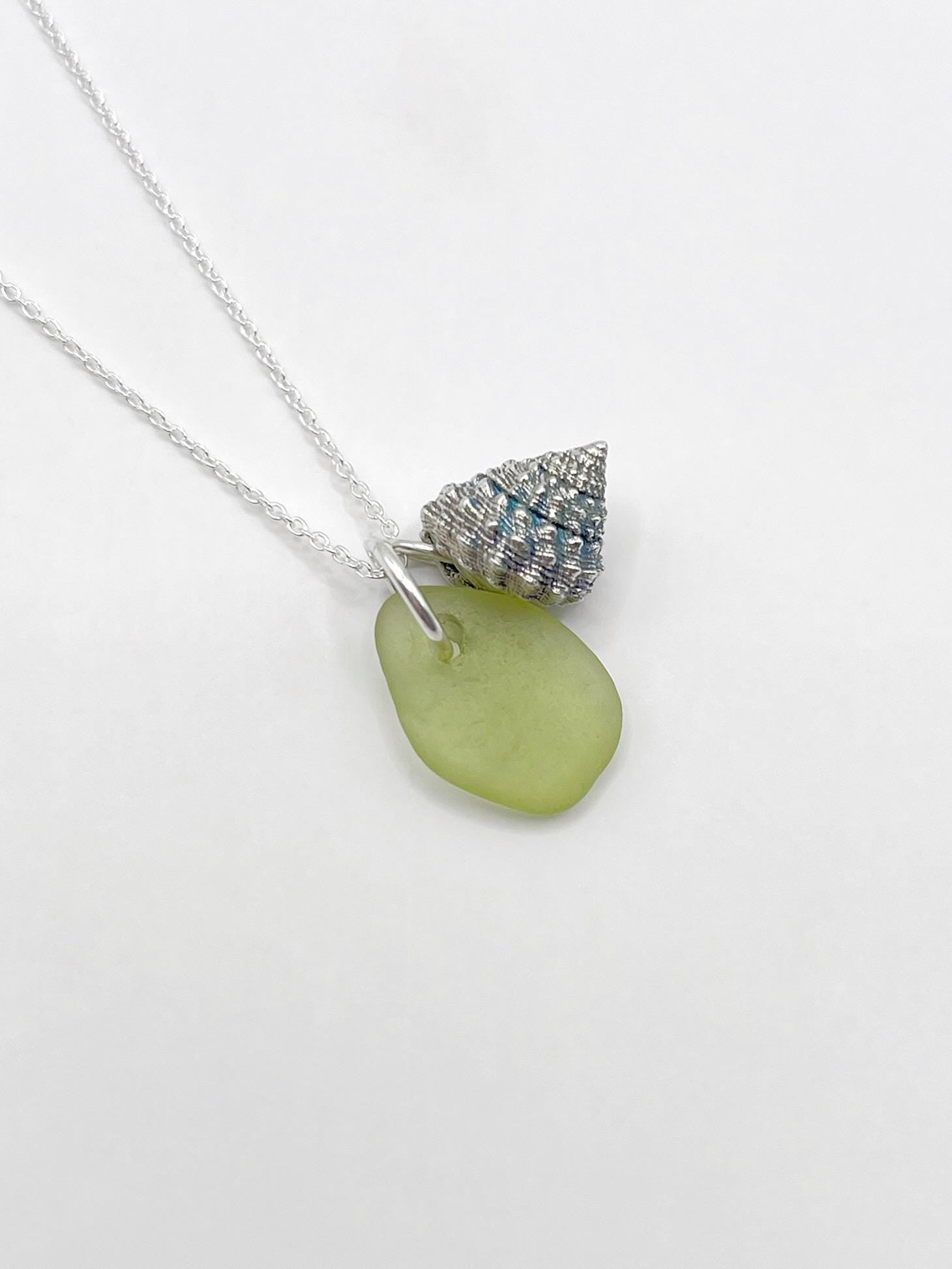 Necklace with lime green sea glass and a silver shell charm laid on a white background