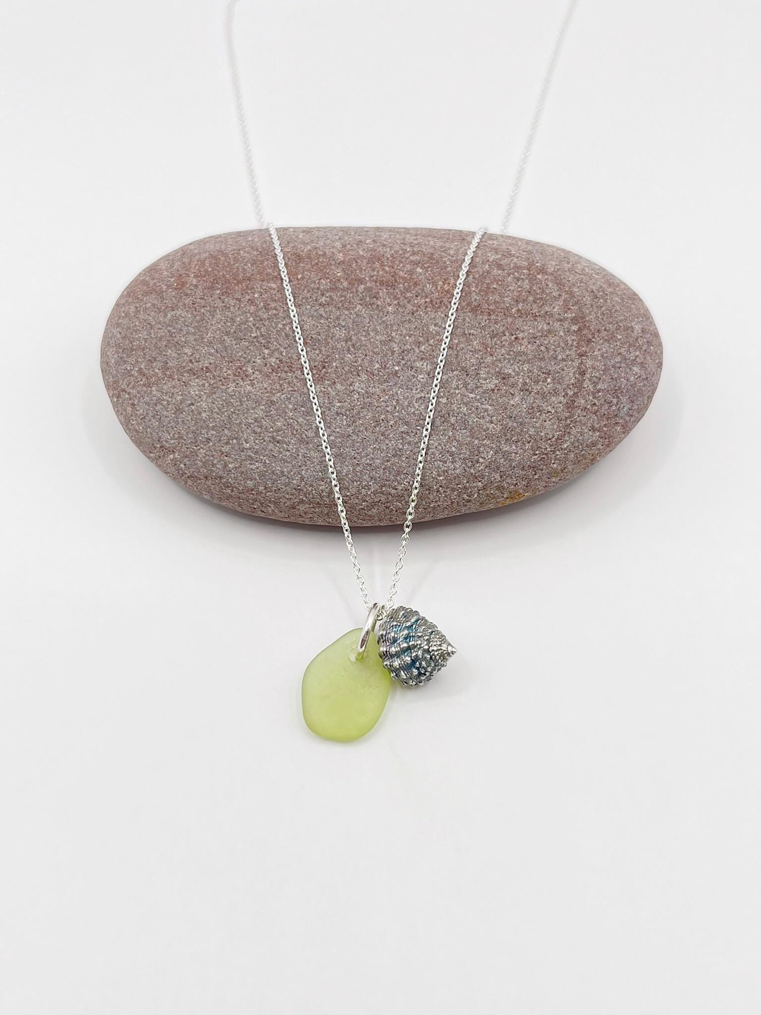 Necklace with lime green sea glass and a silver shell laid on a white background