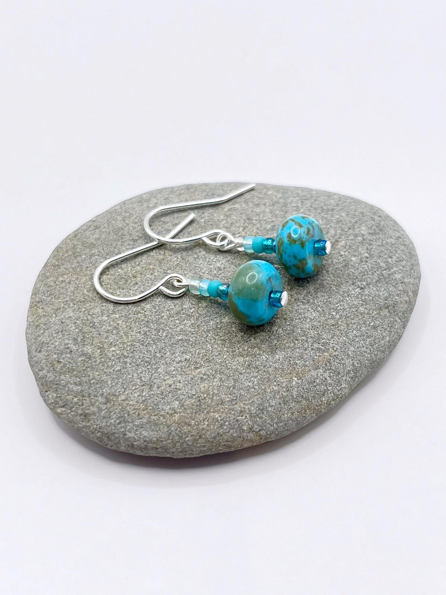 Turquoise beaded earrings on a grey pebble with a white background