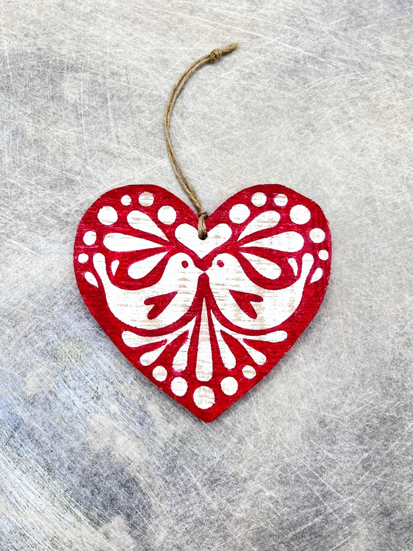 Red heart-shaped wooden hanging decoration with folk style love bird print   laid on a textured surface.