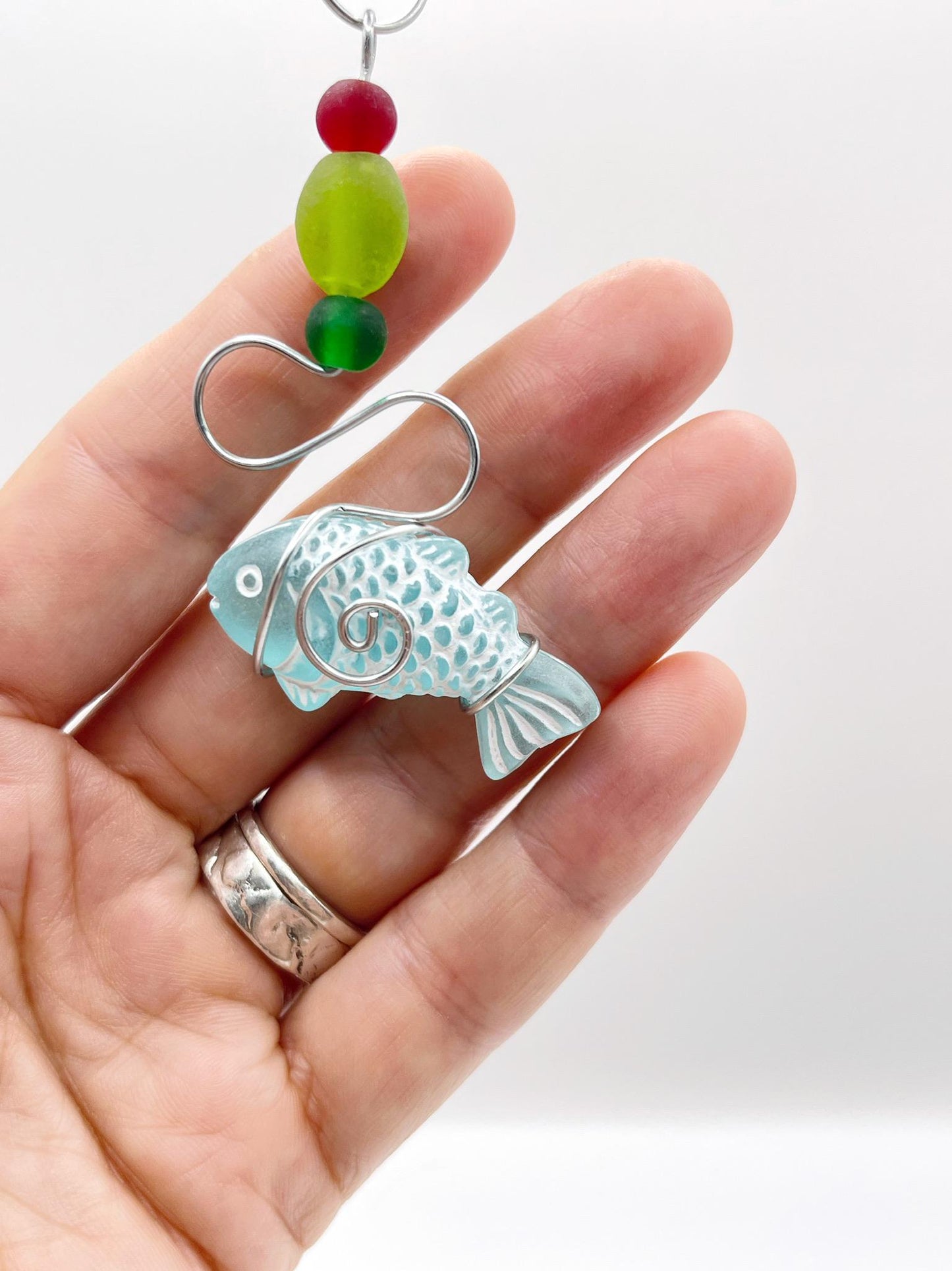 Decorative hanging ornament with a fish design, wire and colourful beads held in a hand against a white background