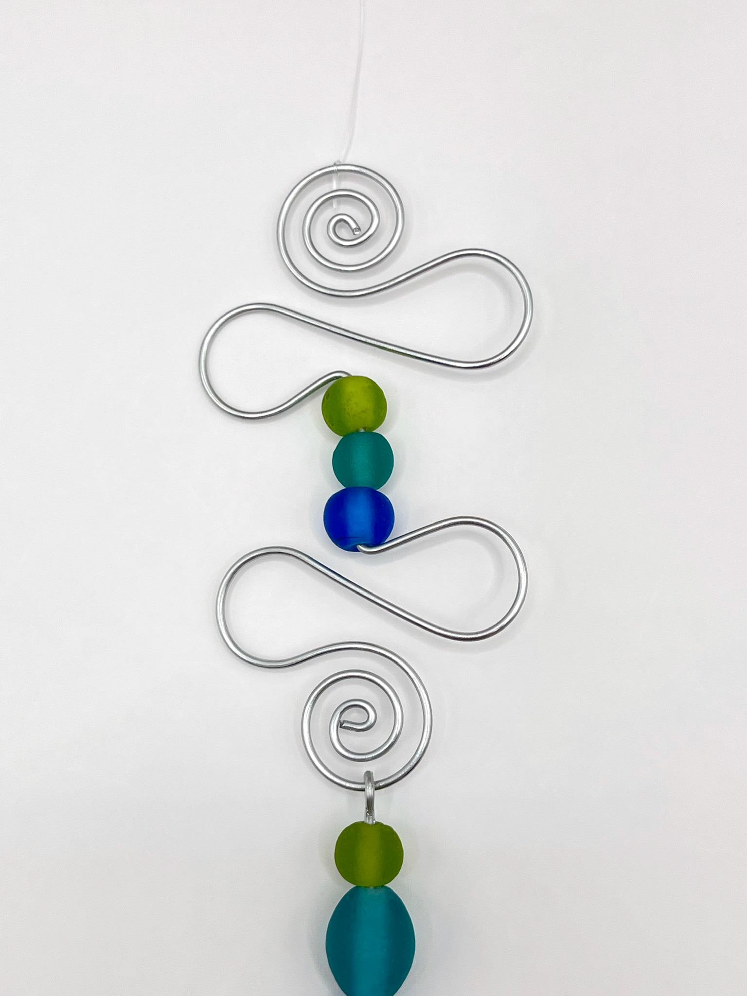 Close up of decorative hanging ornament with blue fish, wire and colourful beads on a white background