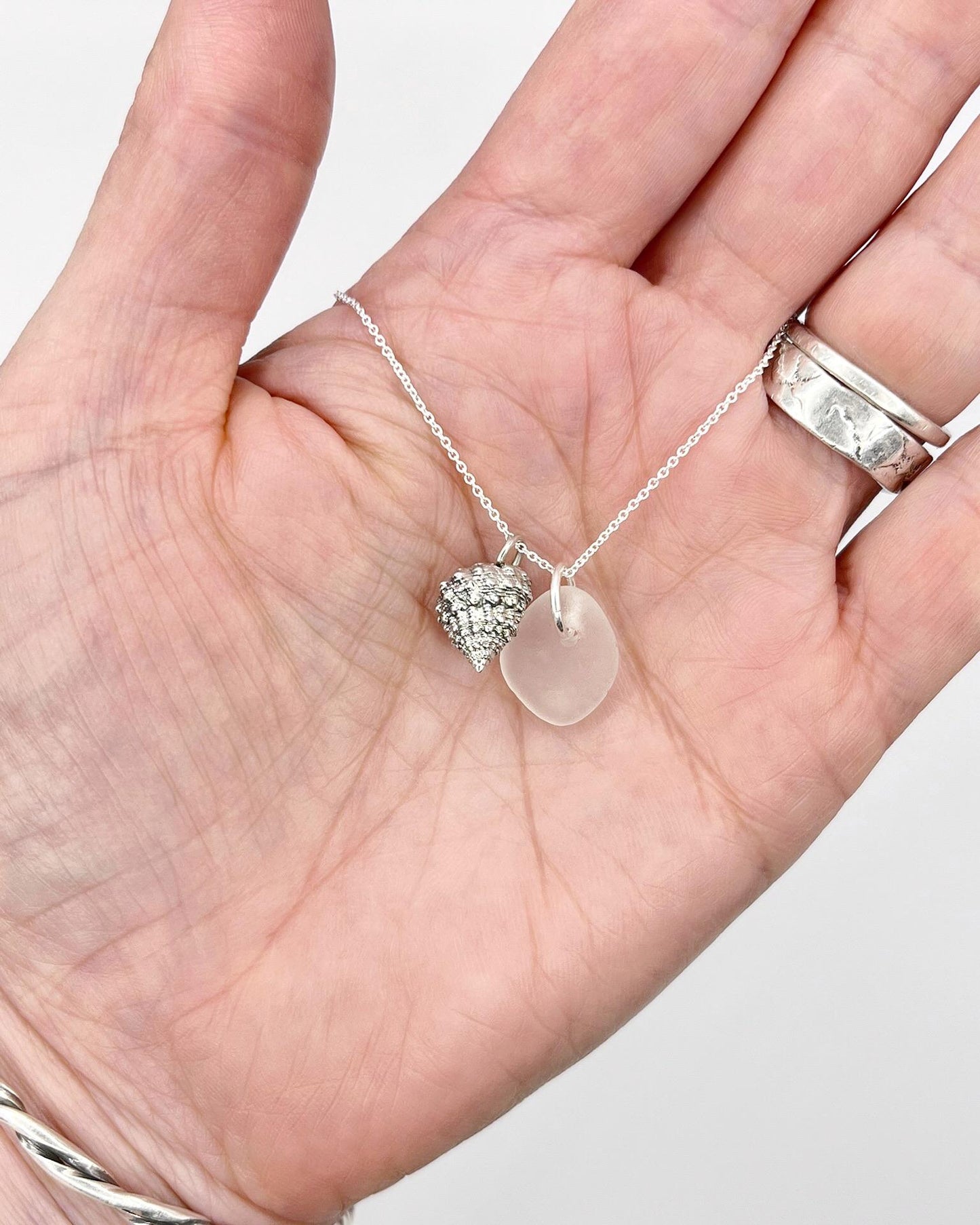 Silver necklace with White Sea glass and silver shell pendant held in a hand against a white background