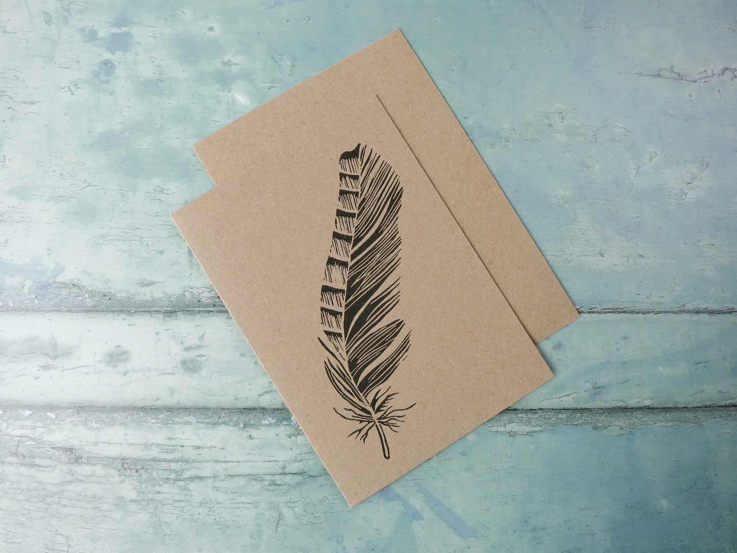 Kraft paper card with an original feather lino print laid on a textured blue surface