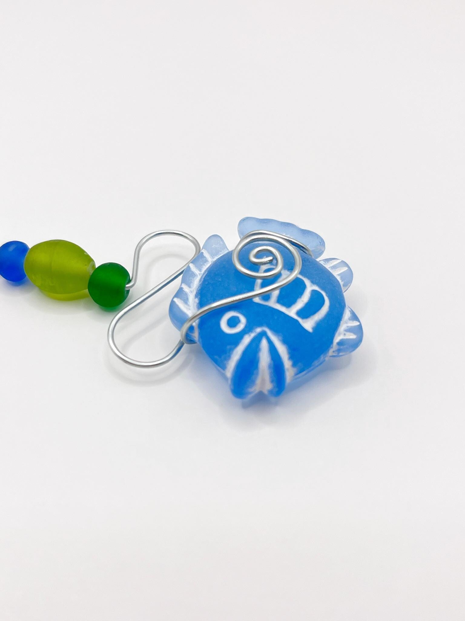 Close up of decorative hanging with blue fish, wire and colourful beads on a white background