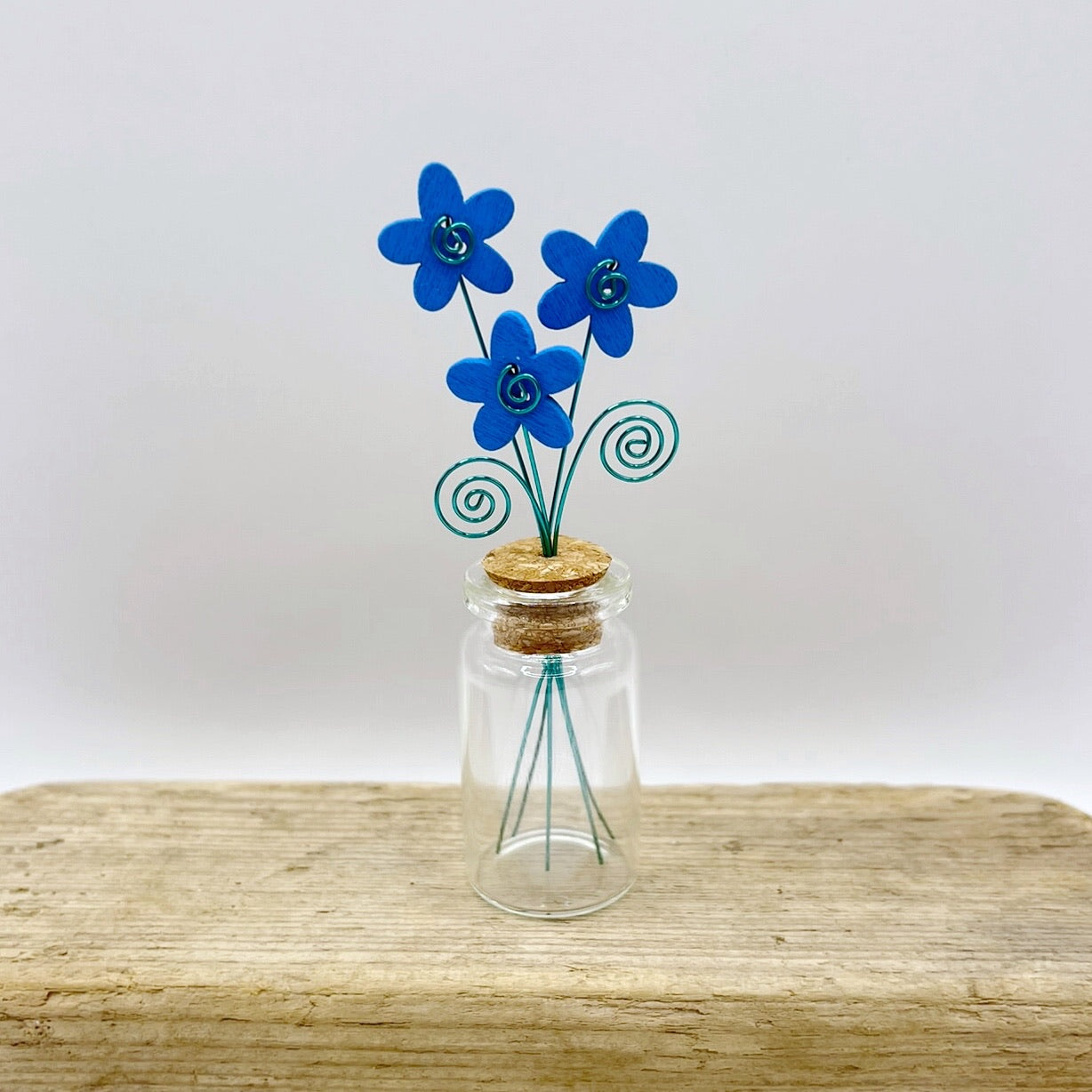 Little glass bottle with three blue wooden flowers sat on driftwood